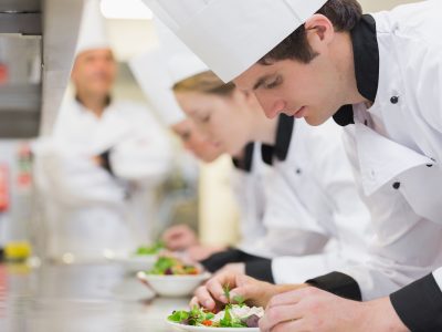 Culinary class in kitchen making salads as teacher is overlooking